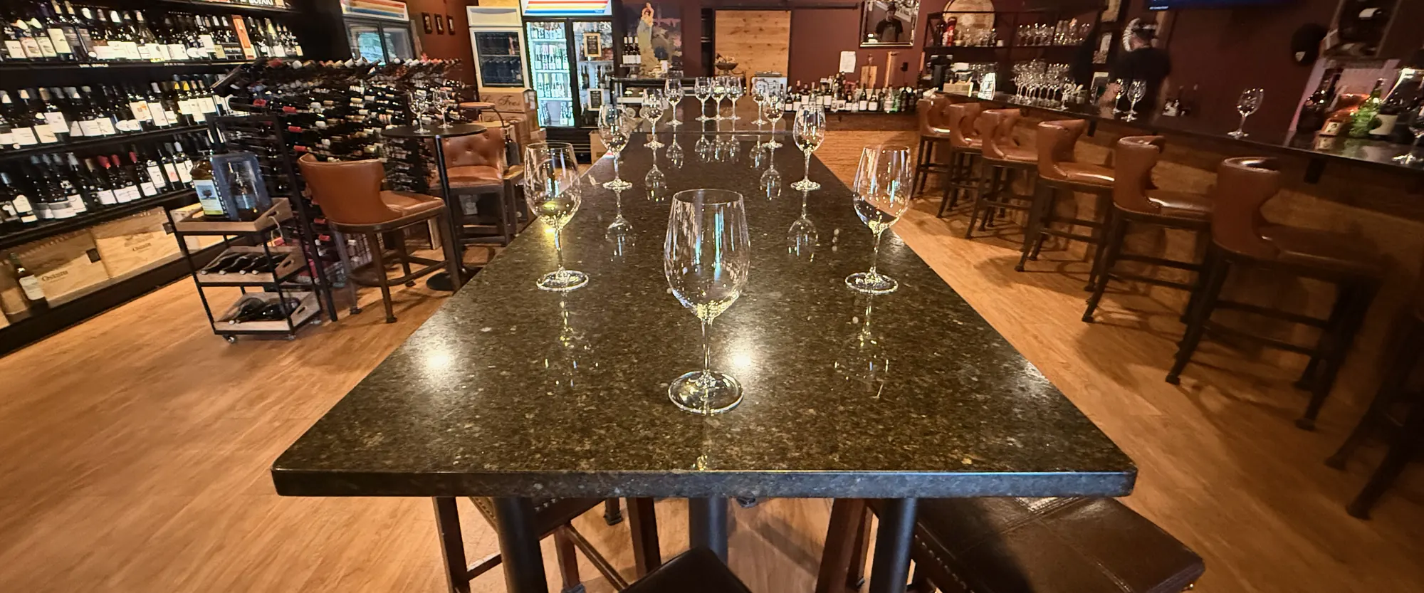 The long granite table at La Vid set with wine glasses, leather bar stools along the bar, and wine walls down both sides of the room