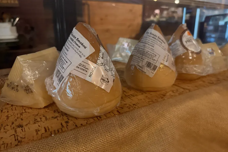 Wedges and rounds of Spanish cheese, wrapped and labeled, on a burlap-covered counter at La Vid