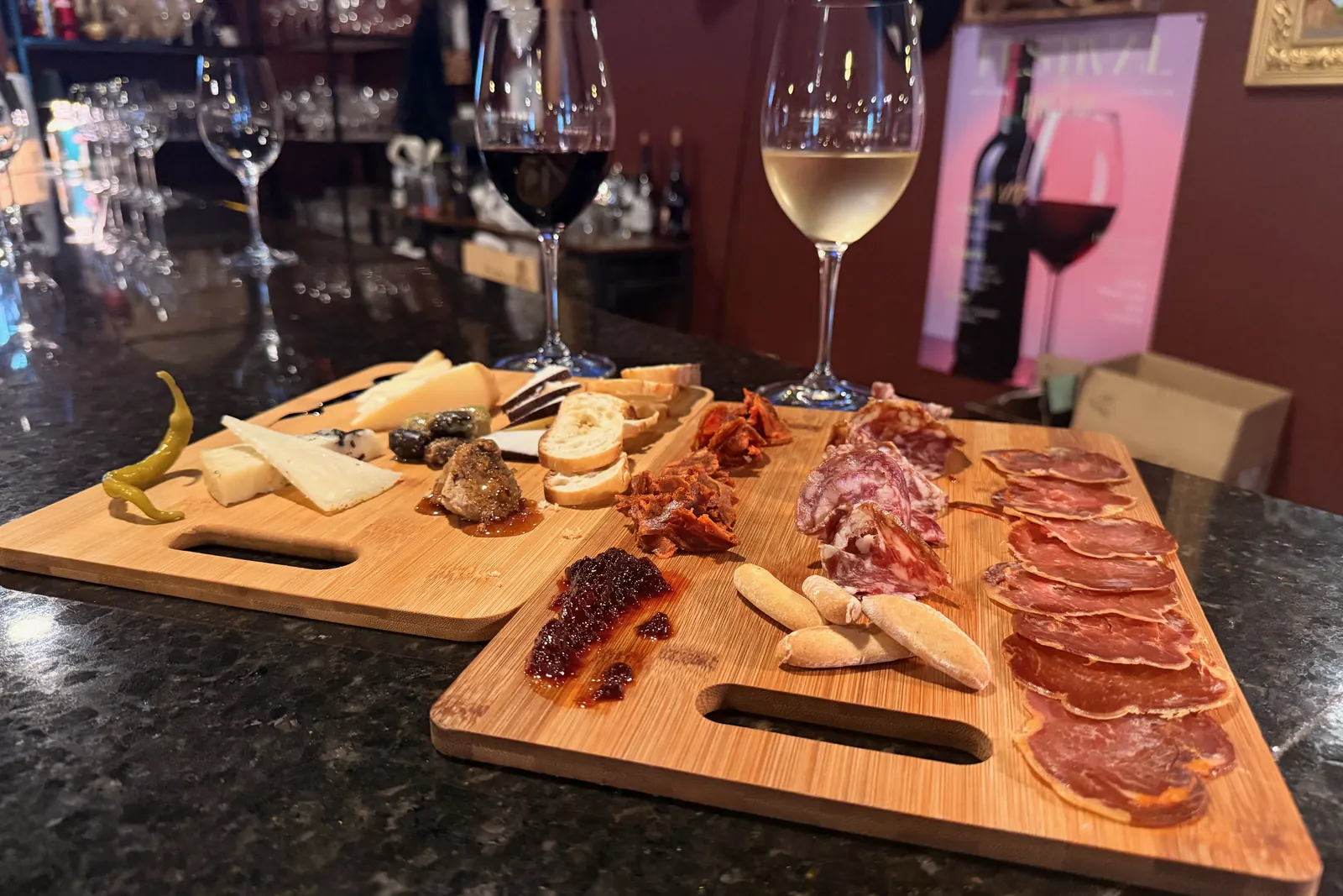 The Deluxe Tabla de la Casa on the bar at La Vid: two wooden boards of sliced lomo, salchichón, and chorizo ibérico, wedges of sheep’s milk, goat, and smoked cheese, blue cheese with truffle honey, La Vid olives, guindilla peppers, picos breadsticks, baguette slices, and fruit marmalade, beside a glass of red and a glass of white
