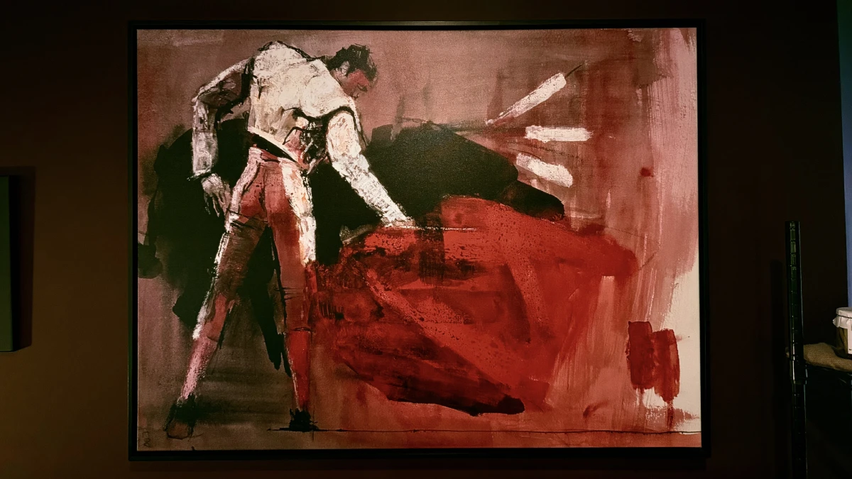 A framed expressionist painting of a matador sweeping a red cape, hanging on the wall at La Vid