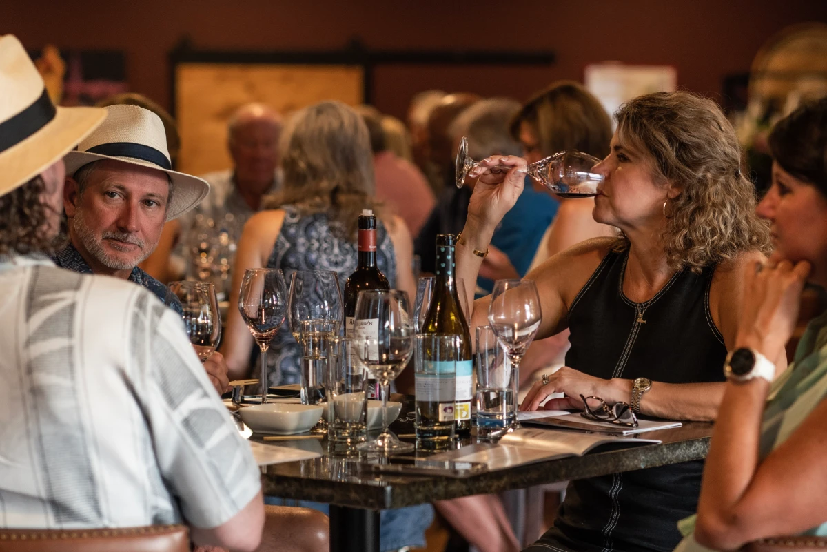 Guests at a full table at La Vid, glasses and open bottles between them, one raising a glass of red to taste