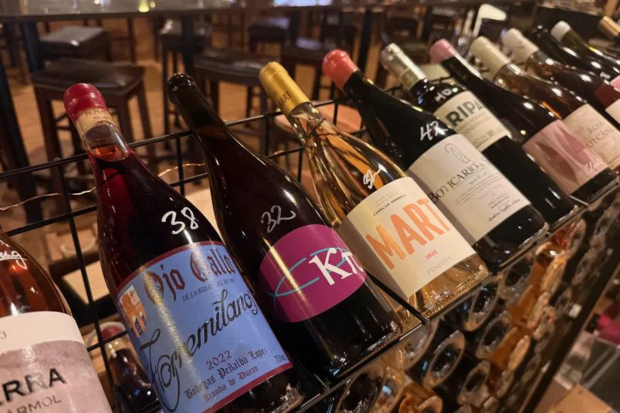 Rosados racked at an angle at La Vid: bottles in shades from pale salmon to deep pink, with handwritten prices